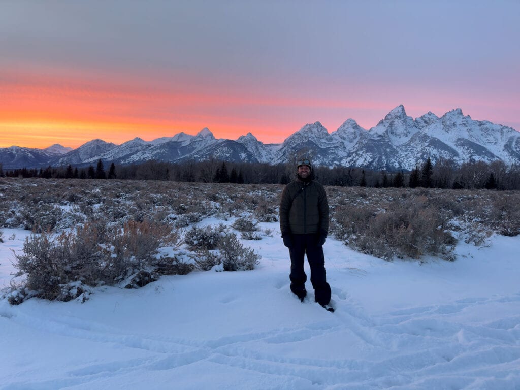 Kyle Dropik standing in the snow at sunset beneath the Grand Teton mountain range
