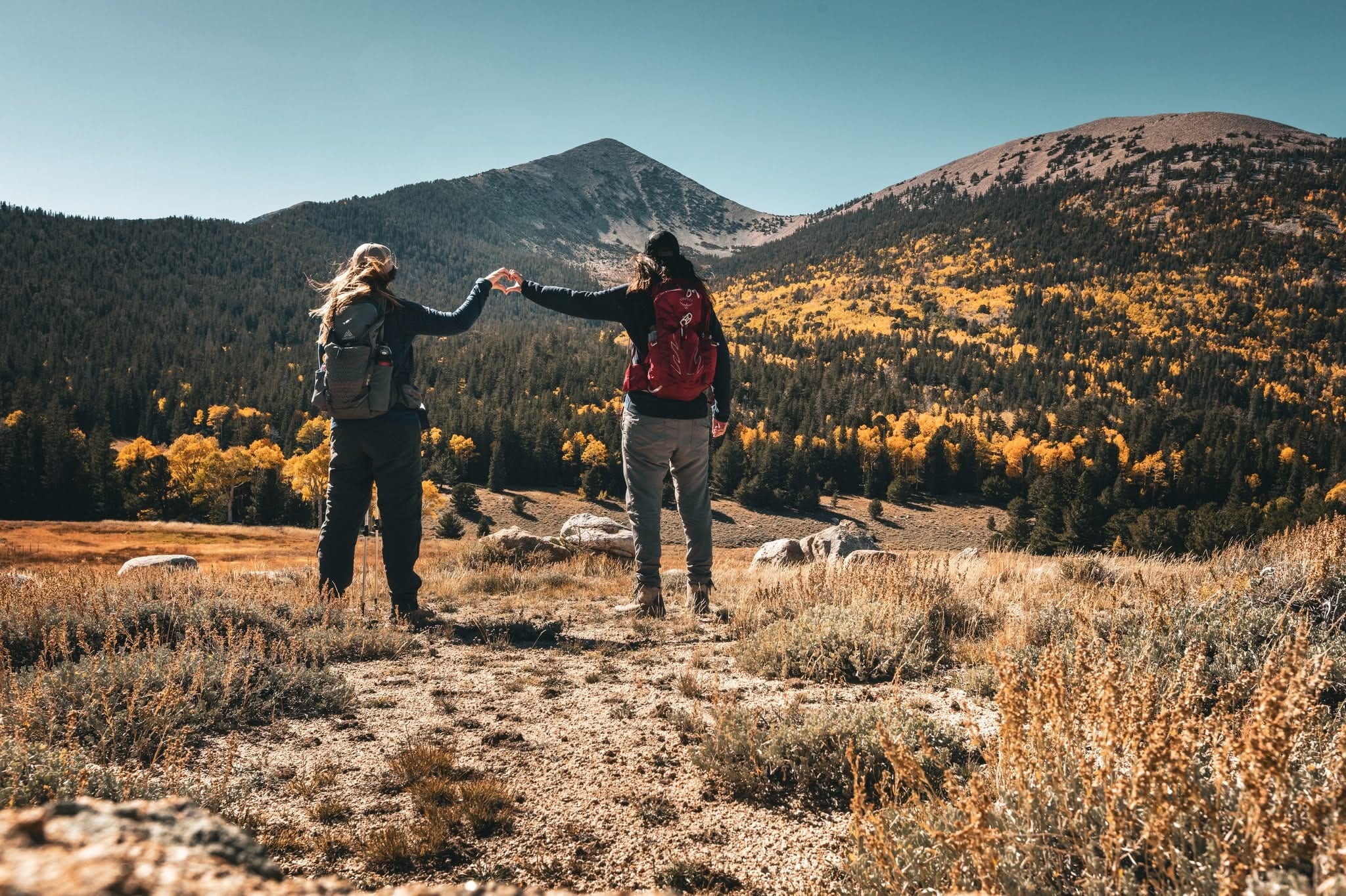 Sarah Moore and her wife forming a heart shape with their hands while hiking in the mountains
